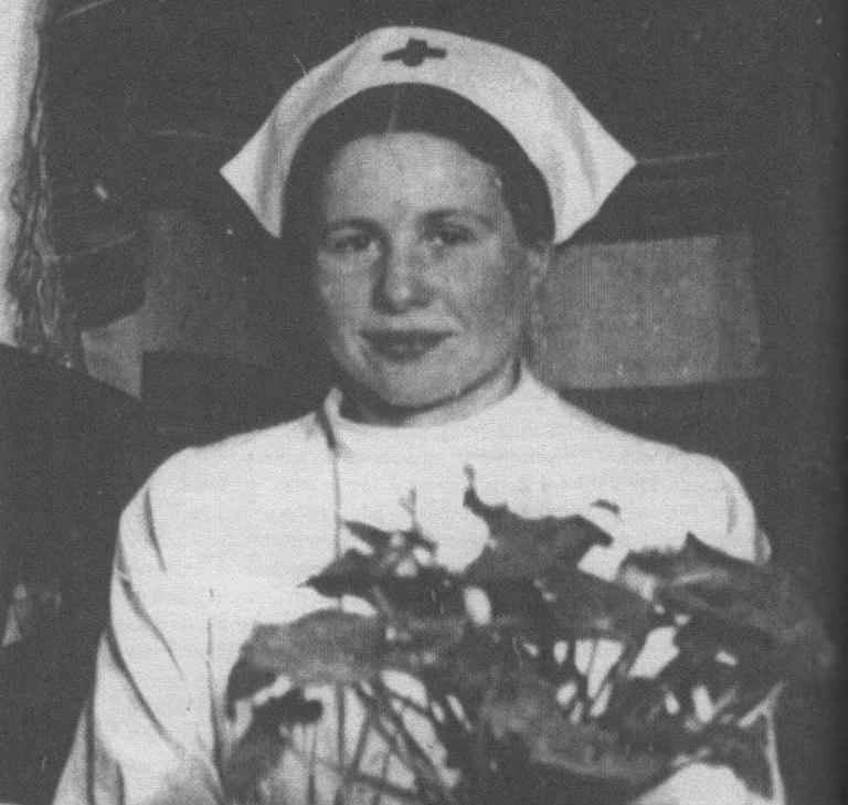 La imagen muestra a Irena Sendler vestida con un uniforme de enfermera, que incluye un tocado con una cruz roja, y sostiene lo que parece ser una planta. La fotografía es en blanco y negro y es probablemente de mediados del siglo 20 o antes.